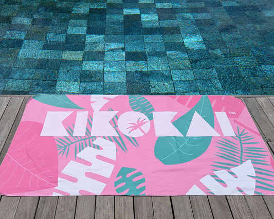 Microfibre towel with a jungle print in pink, green, and white, laid out on a wooden surface by a pool.